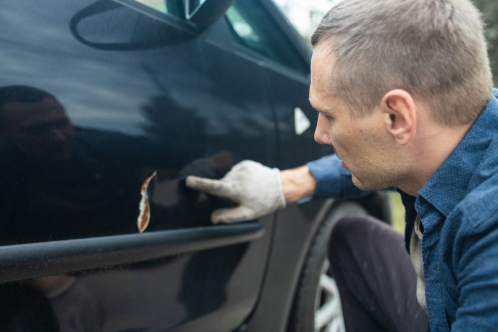 Mid adult man checking his car for scratches and dents. Scratches on the car door. Car accident. Aut