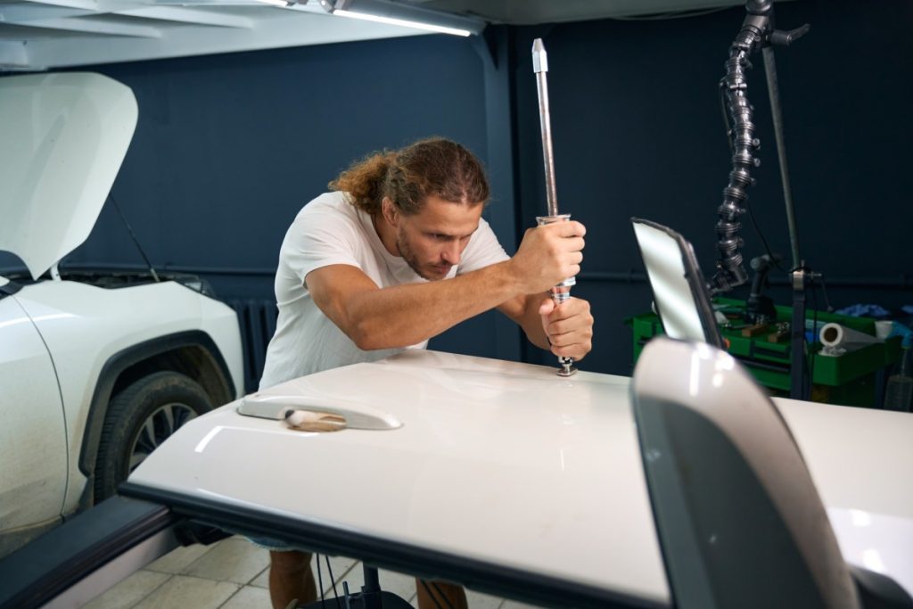 Man uses a special tool to level out body dents